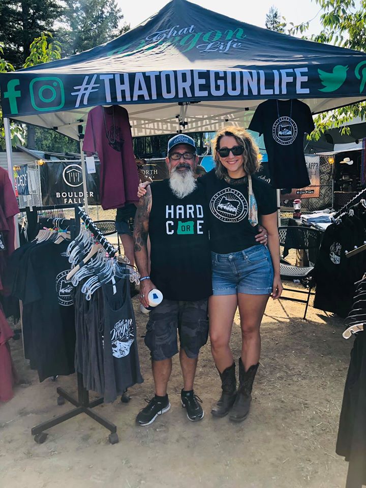 Two people wearing That Oregon Life apparel beneath the brand’s tent at an outdoor event