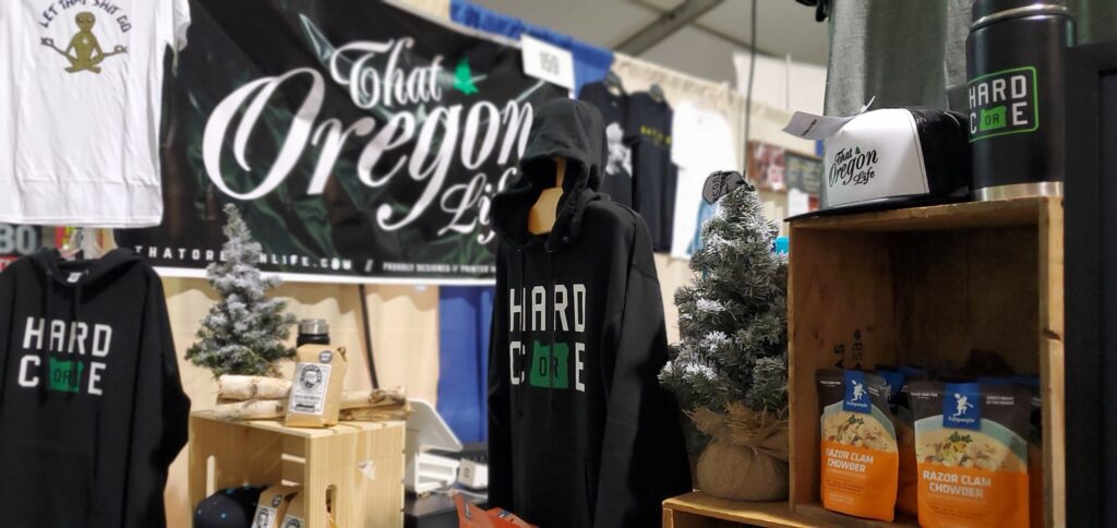 That Oregon Life event booth with Hardcore hoodies, hats, and a large brand banner