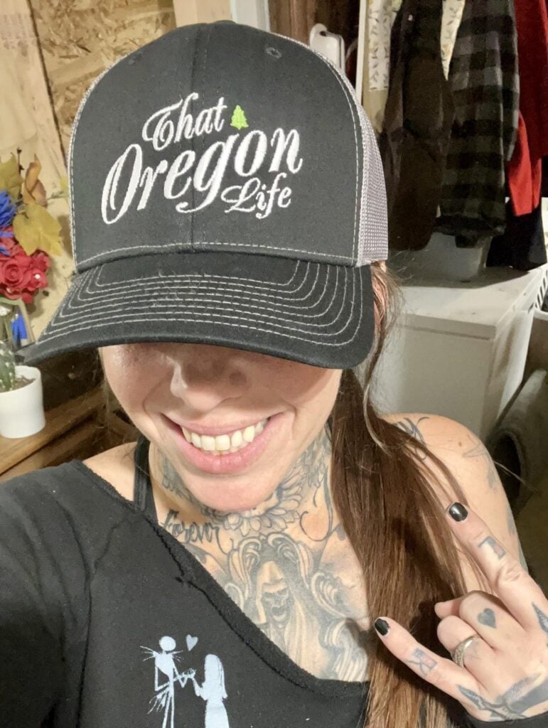 Smiling woman wearing an embroidered That Oregon Life trucker hat