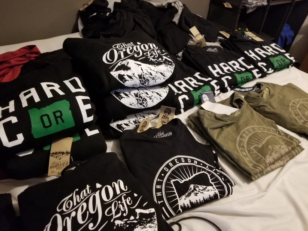 Folded That Oregon Life mountain and Hardcore graphic apparel on a market table