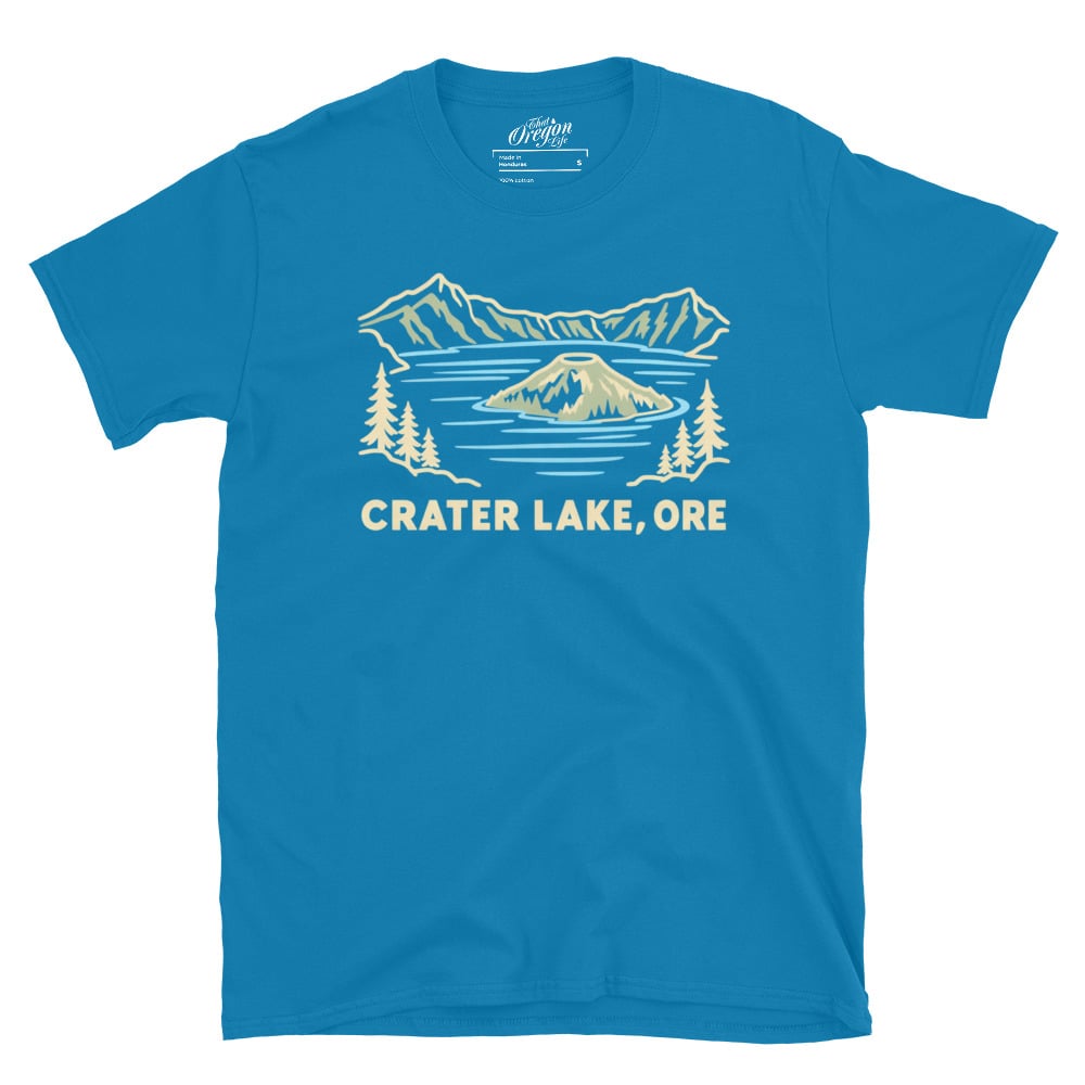 Sapphire blue Crater Lake Oregon tee with pale line art of Wizard Island, mountains, evergreen trees, and CRATER LAKE, ORE lettering.
